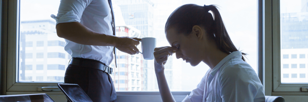When Work Knowingly Makes Your Physical and Mental Health Worse A woman sitting at her laptop with her hand to her head, looking stressed.