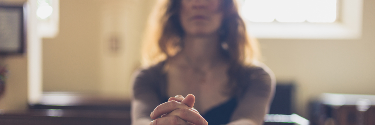 When Religion and Spirituality Are Used to Blame Those With Illness woman sitting in a pew at church with her hands folded