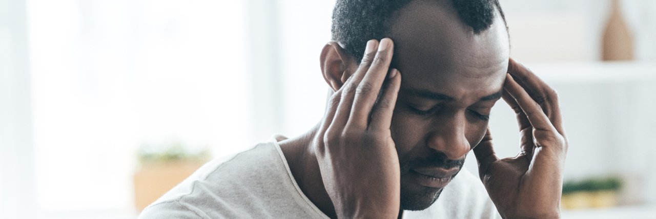 20 Things ME/CFS Post-Exertional Malaise Feels Like A picture of a man with his hands to his head, looking tired.
