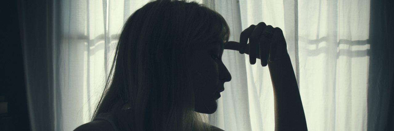 Does the Placebo Effect Help My Migraine? A woman in a dark room with her hand to her head.