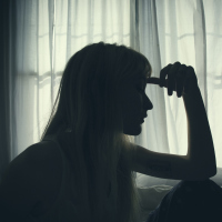 A woman in a dark room with her hand to her head.