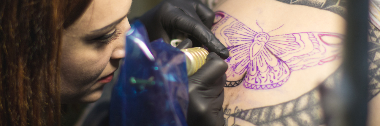 photo of woman tattooing butterfly onto another woman in close up