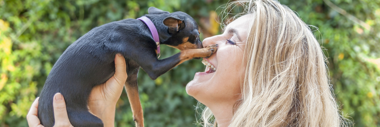 Is It Wise to Have a Pet When You're Chronically Ill? A woman holding up a dog, smiling.