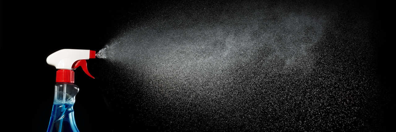 A spray bottle spraying in front of a black background.