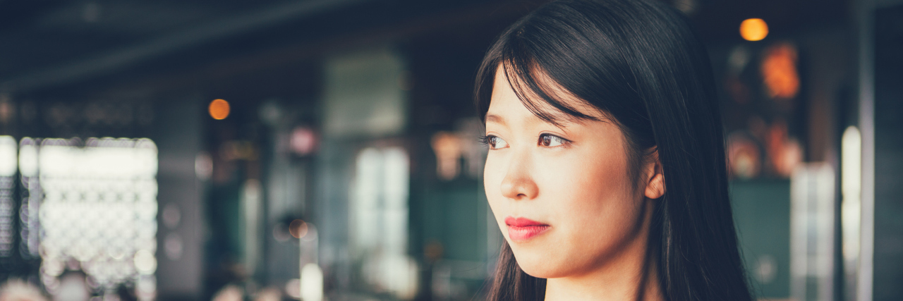 An Asian woman standing in a restaurant, looking away from the camera.