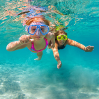 Two girls swim underwater with goggles looking at camera