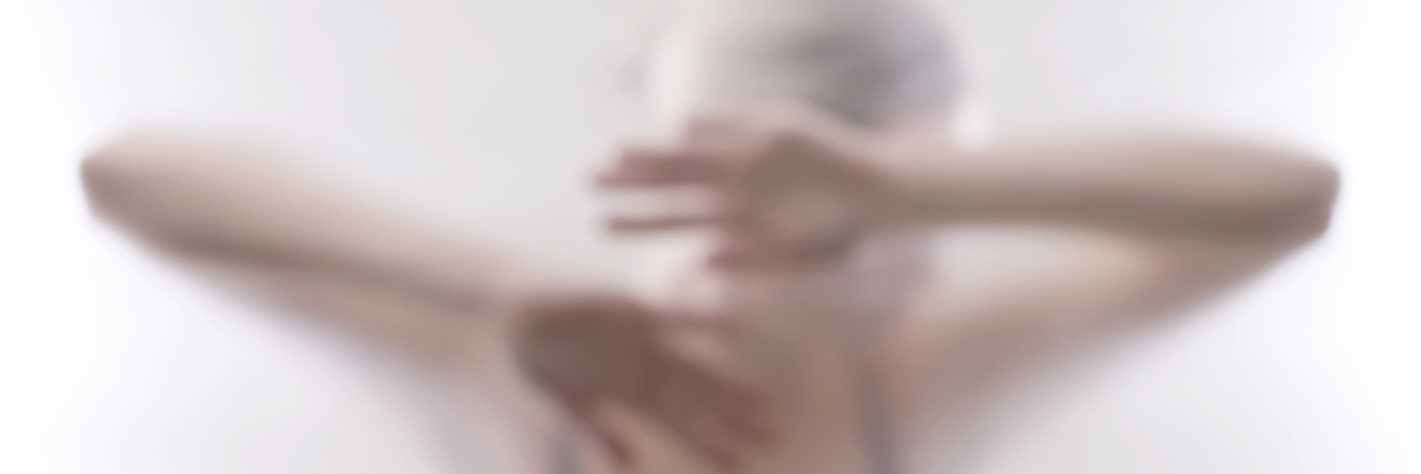 When Chronic Illness Leaves You Trapped in Your Diagnosis A woman behind a plastic wall, her head resting on her arms.