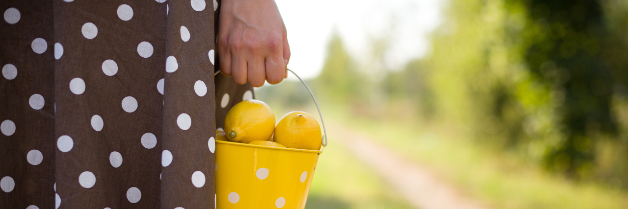 A close-up of a woman holding a yellow bucket of lemons.