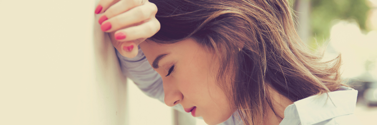 A woman leaning against the wall, looking upset.