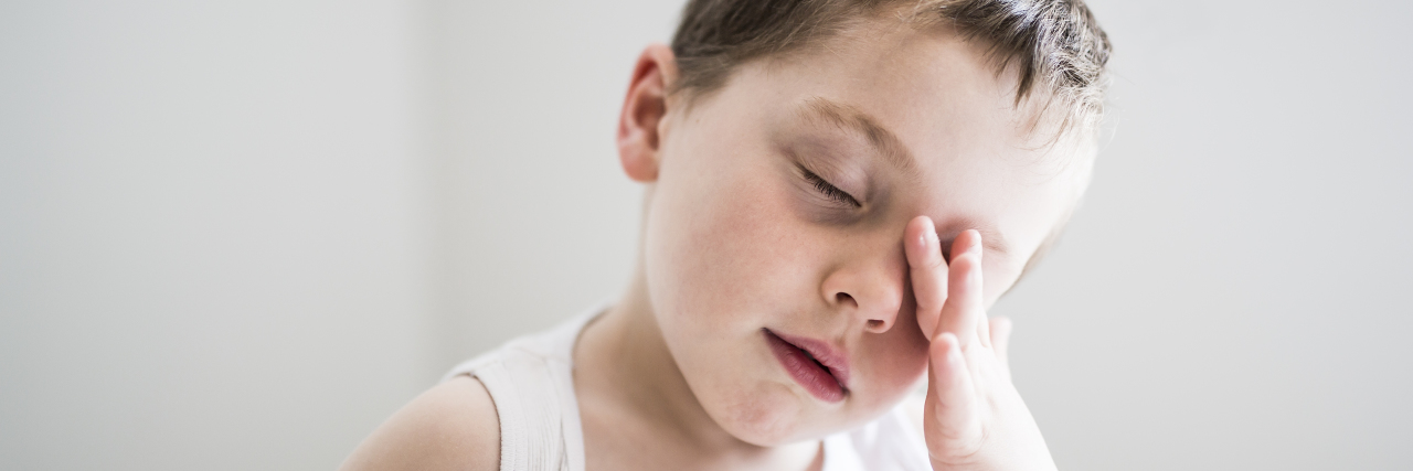 Losing Sleep With Angelman Syndrome boy rubbing his eyes under the covers
