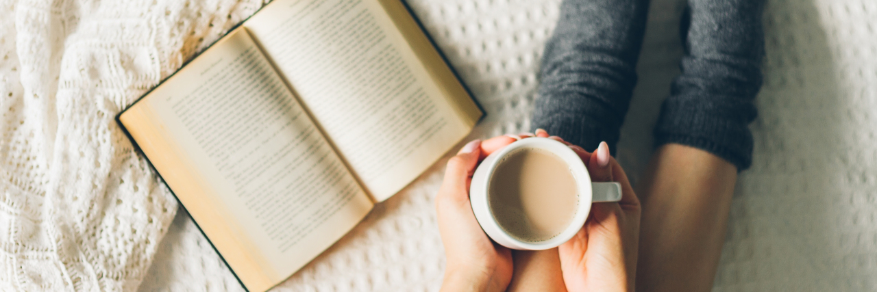 woman laying in bed and read book with cup if coffee