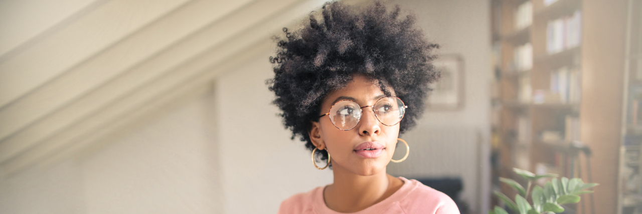 How I Stopped Seeing My Body as the Enemy A woman standing in a room, looking towards a window.