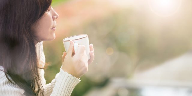 A picture of a woman outside, drinking coffee.