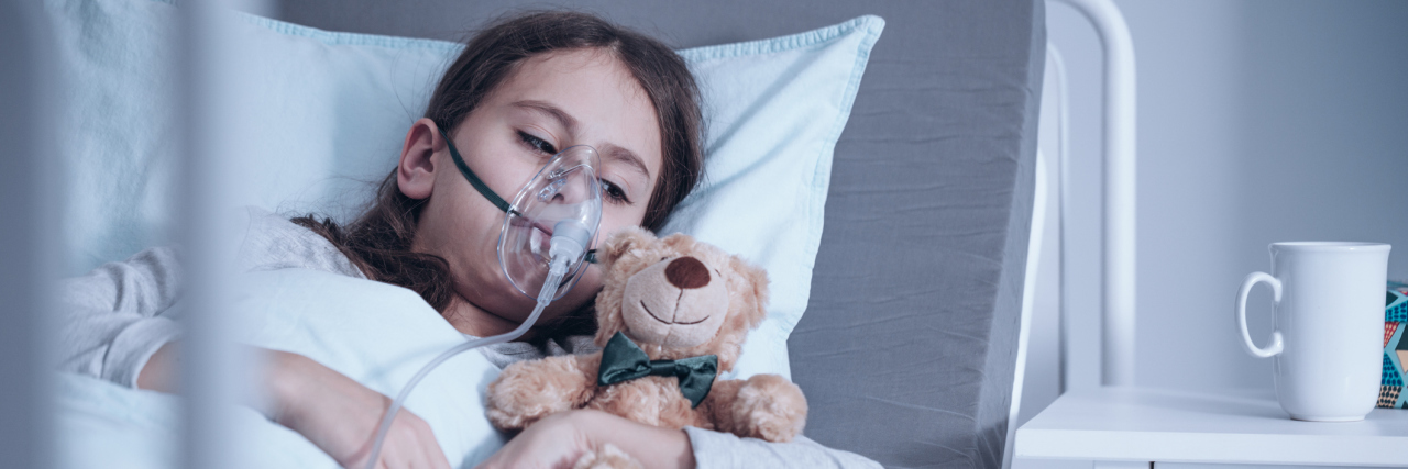 A picture of a child laying in a hospital bed, wearing an oxygen mask.