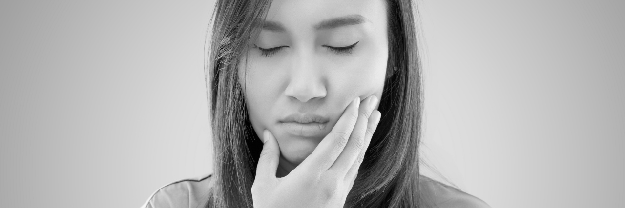black and white photo of woman holding her jaw in pain