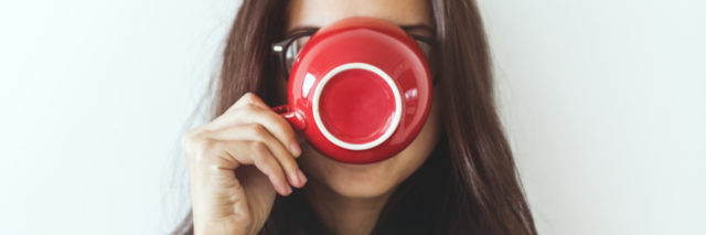 A woman in a sweatshirt drinking out of a red mug