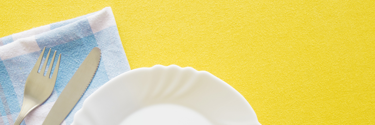 An empty plate and silverware on a yellow background.