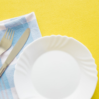 An empty plate and silverware on a yellow background.