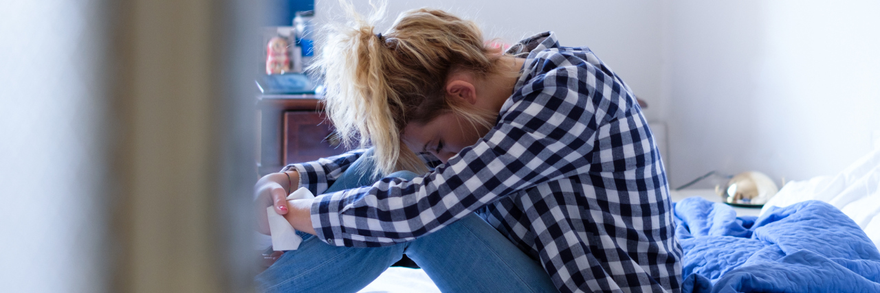 What It's Like to Be a Teenager Who Uses a Catheter A young woman sitting on her ed with her head resting on her knees.