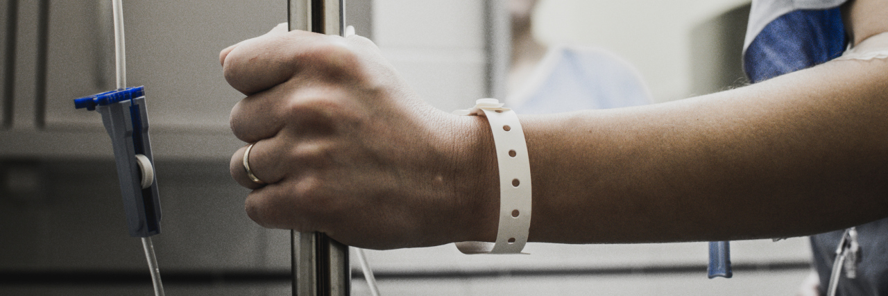 Why I'm Thankful for the Medical Treatment I Originally Never Wanted A patient looking at herself in a mirror. A medical bracelet on her wrist, while she holds onto an IV pole.