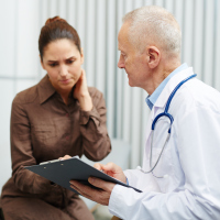 Sad nervous young woman touching neck while reading her medical card shown by senior doctor in lab coat in modern office