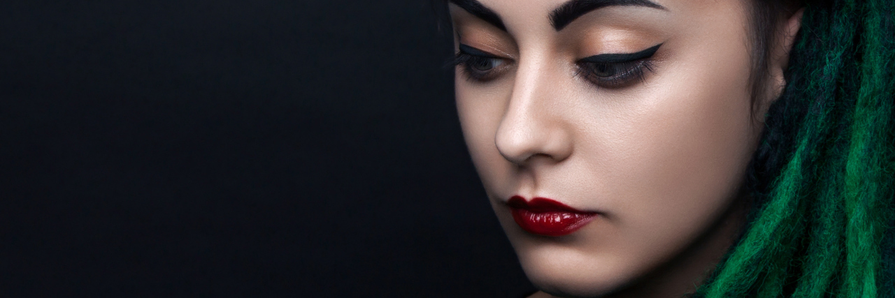 5 Steps I Take When My Body Doesn't Feel Like Mine Because of Pain A woman with green hair looking down, away from the camera.