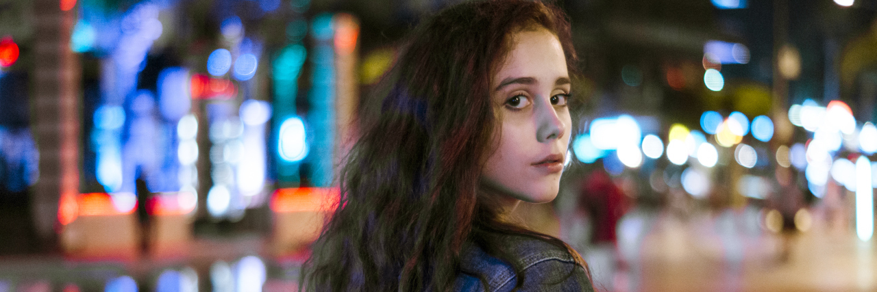 What I Didn't Realize as a Teenager With Epilepsy A woman in a city at night time, looking back at a camera.