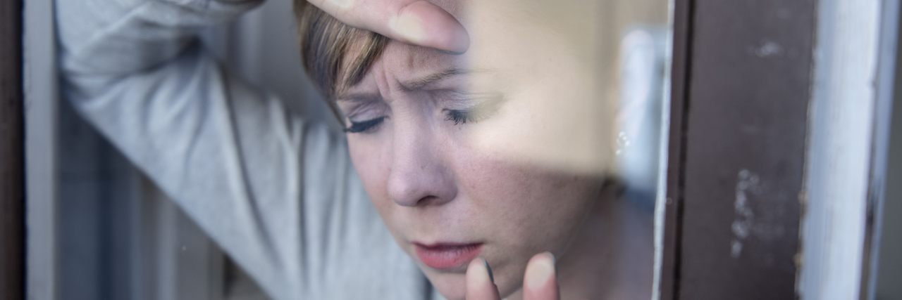 What It's Like Living With Myalgic Encephalomyelis A tired woman leaning her head on a glass door.