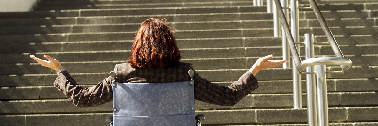 Why We Shouldn't Excuse Inaccessibility Woman in a wheelchair at the bottom of a flight of stairs.