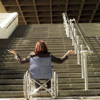 Woman in a wheelchair at the bottom of a flight of stairs.