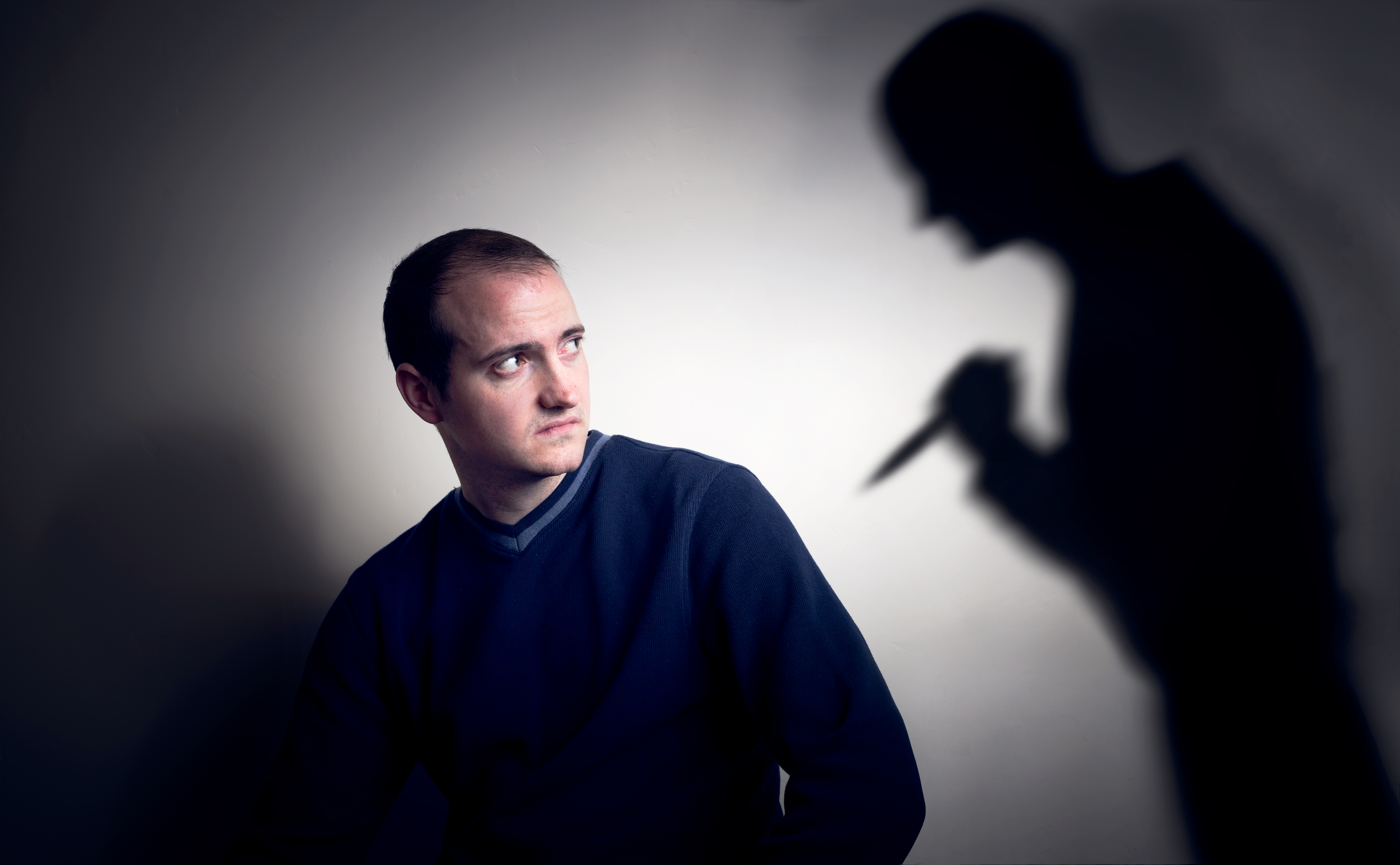 man looking afraid while shadow lurks behind him with a knife - photo by Laurence Boswell of Only Human Photography