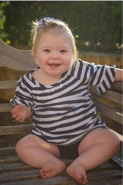 Smiling toddler with Down syndrome wearing a stripped navy and white shirt