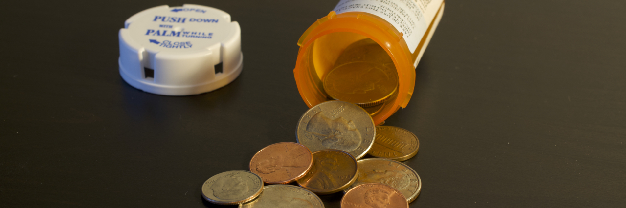 A pill bottle on its side, with money spilling out of it.