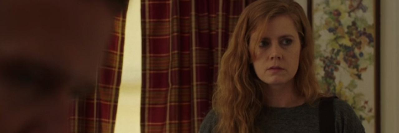 Amy Adams in Sharp Objects. Her character takes notes in a note pad standing in front of the window