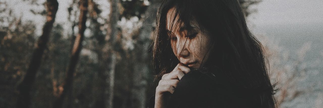 young asian woman looking depressed in front of trees