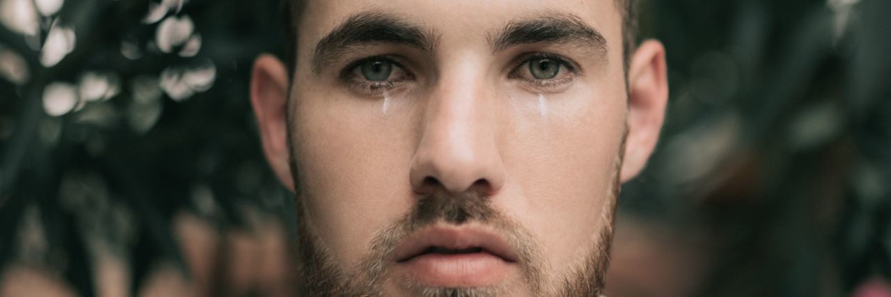 man standing in front of flowers looking into camera and crying