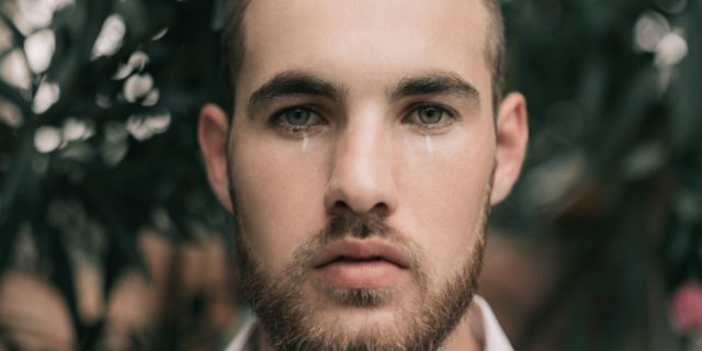 How I'm Breaking the Cycle of Toxic Masculinity for My Sons and Mental Health man standing in front of flowers looking into camera and crying