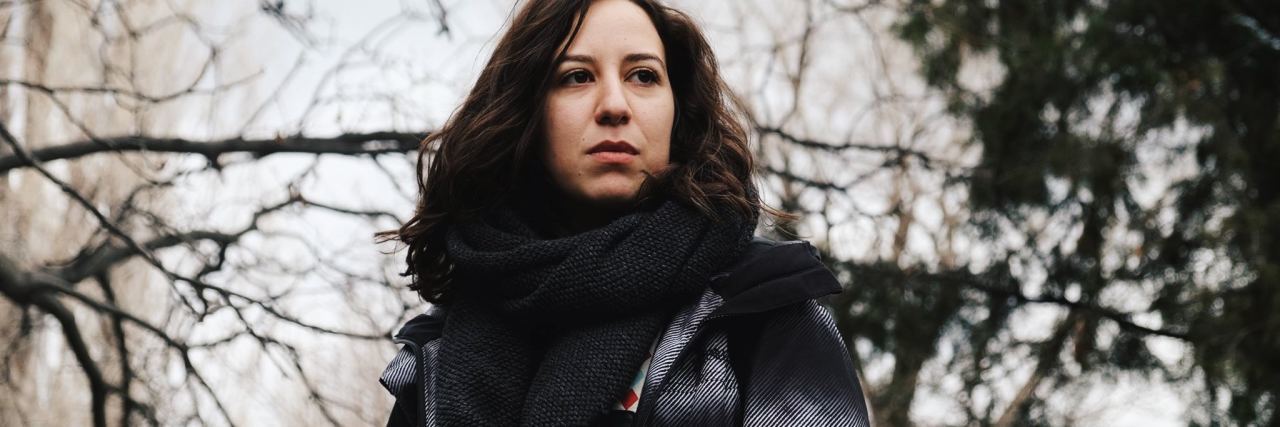 dark haired woman looking worried standing in front of trees