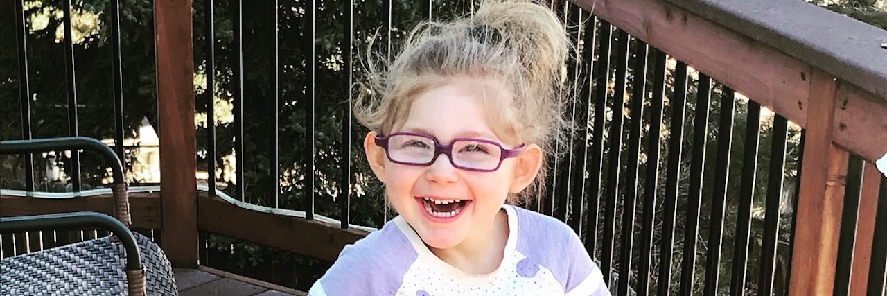 Dear Teachers, Please Presume Competence When You Work With My Child Adorable little girl using yellow walker, she is wearing glasses and giving a big smile at the camera.