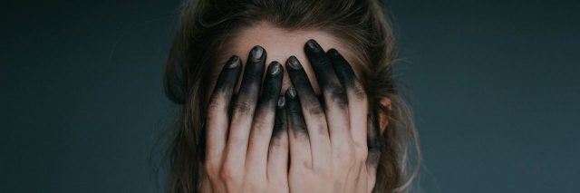 woman covering face with hands stained with black ink