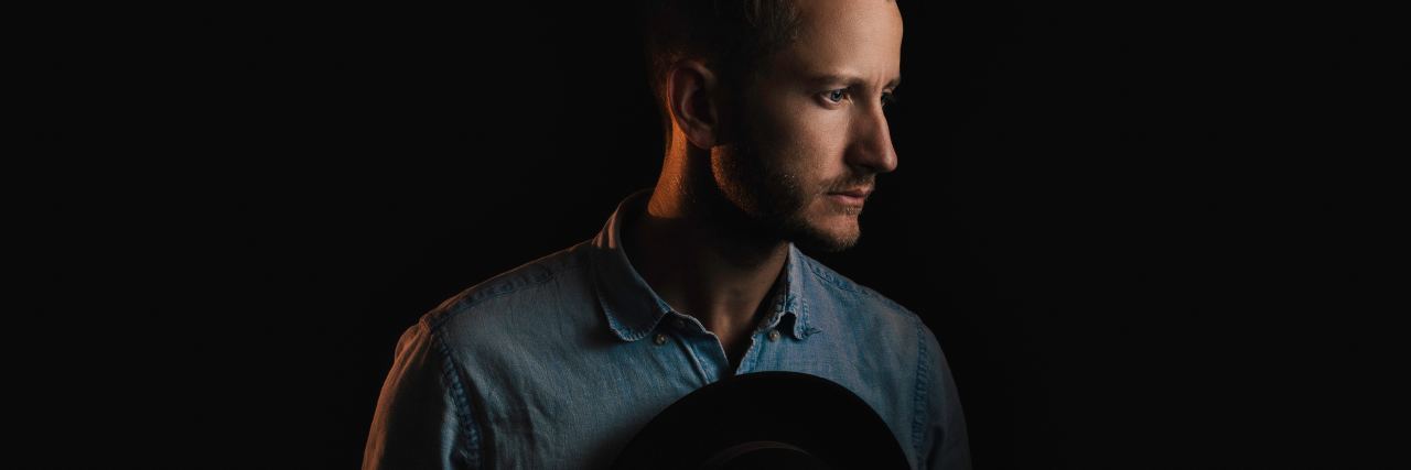 How I Learned to Be Open About Men's Mental Health Writing man standing in darkness holding hat to chest