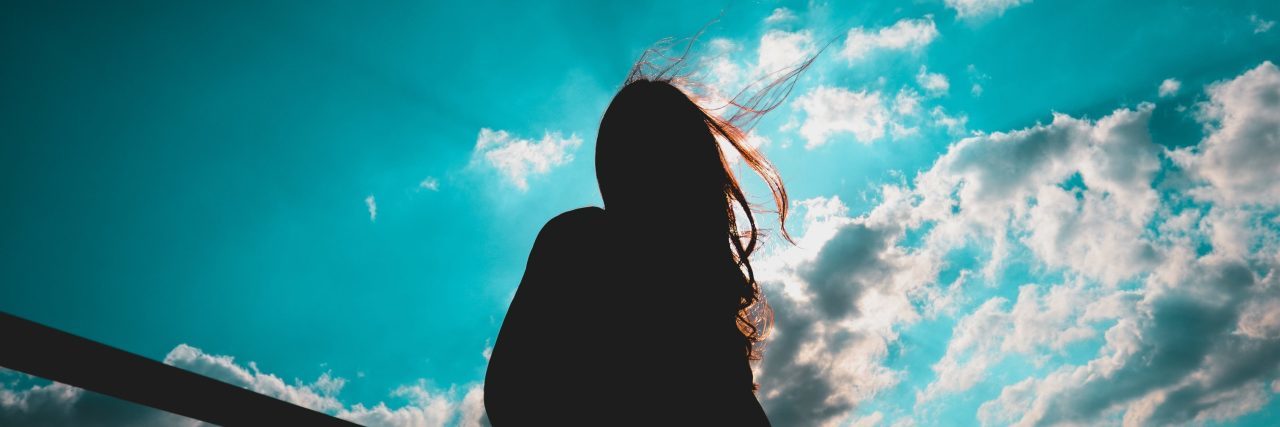 What to Do If You're Having an Anxiety Attack woman silhouetted against vibrant blue sky and white clouds