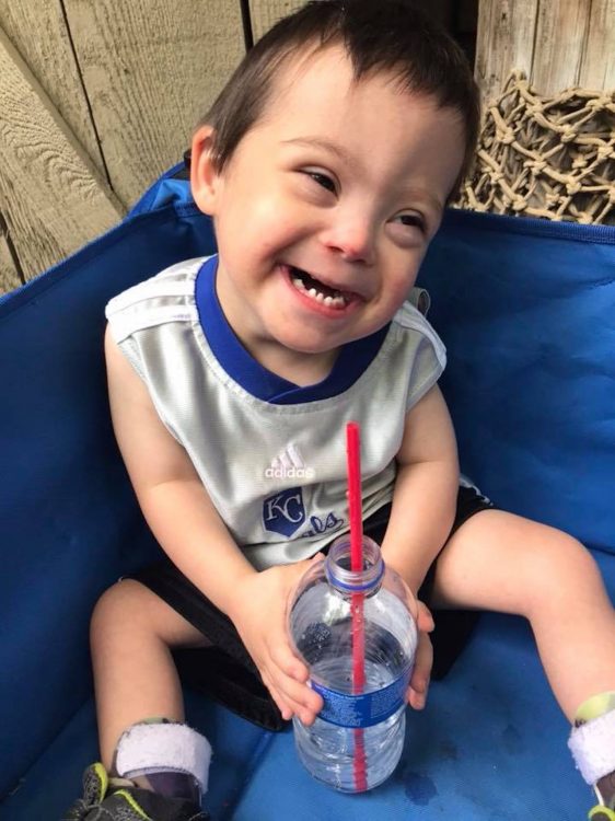 Little boy with Down syndrome smiling at camera, he holds a water bottle with a red straw