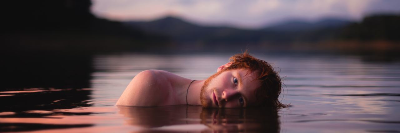 man mostly submerged in lake waster in sunset or sunrise light looking into camera