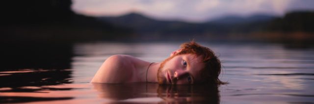 man mostly submerged in lake waster in sunset or sunrise light looking into camera