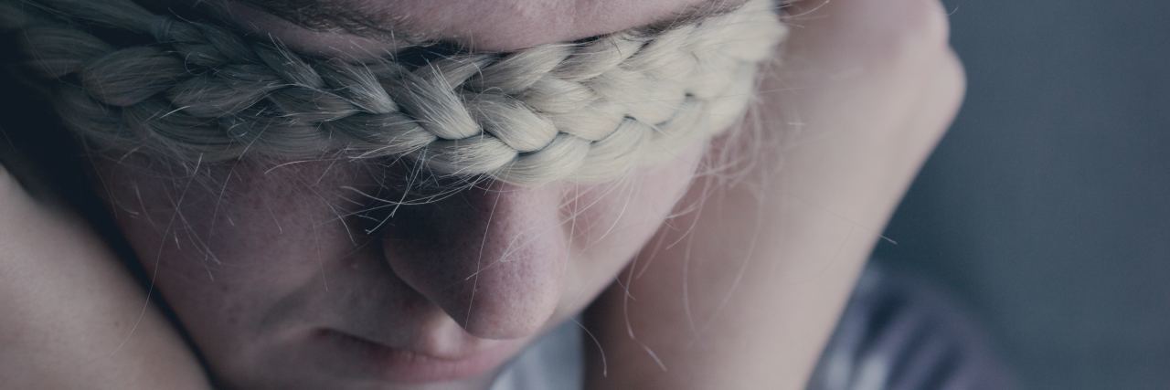 young blonde woman covering eyes with hair braid