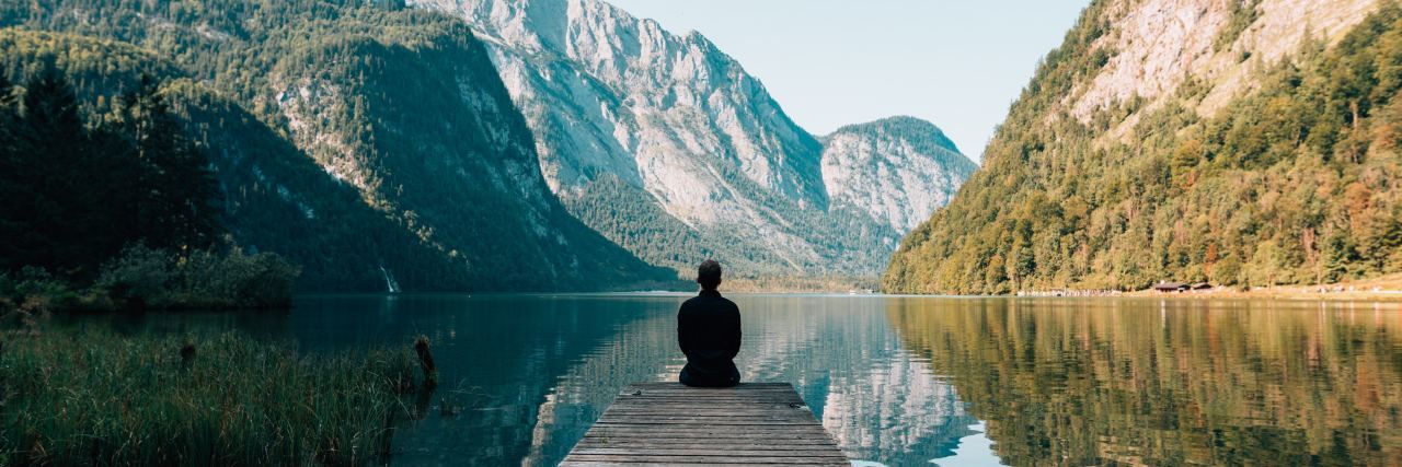 How to Start Practicing Meditation for Beginners person sitting on a big rock overlooking a lake
