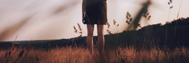 young woman standing in field alone at sunset