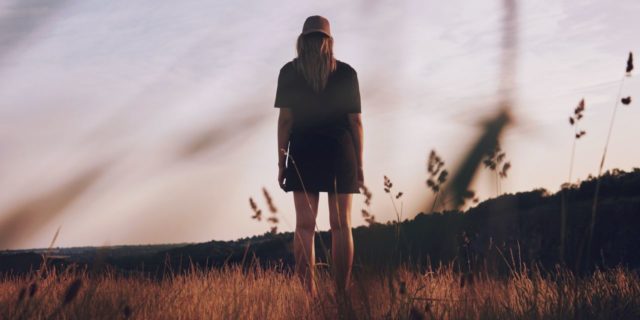 young woman standing in field alone at sunset