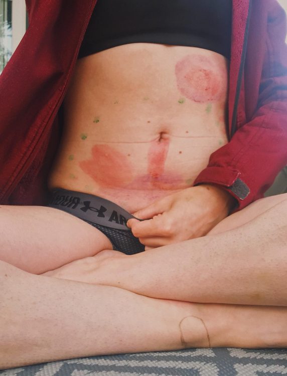 woman sitting with stomach painted in two sections with red paint